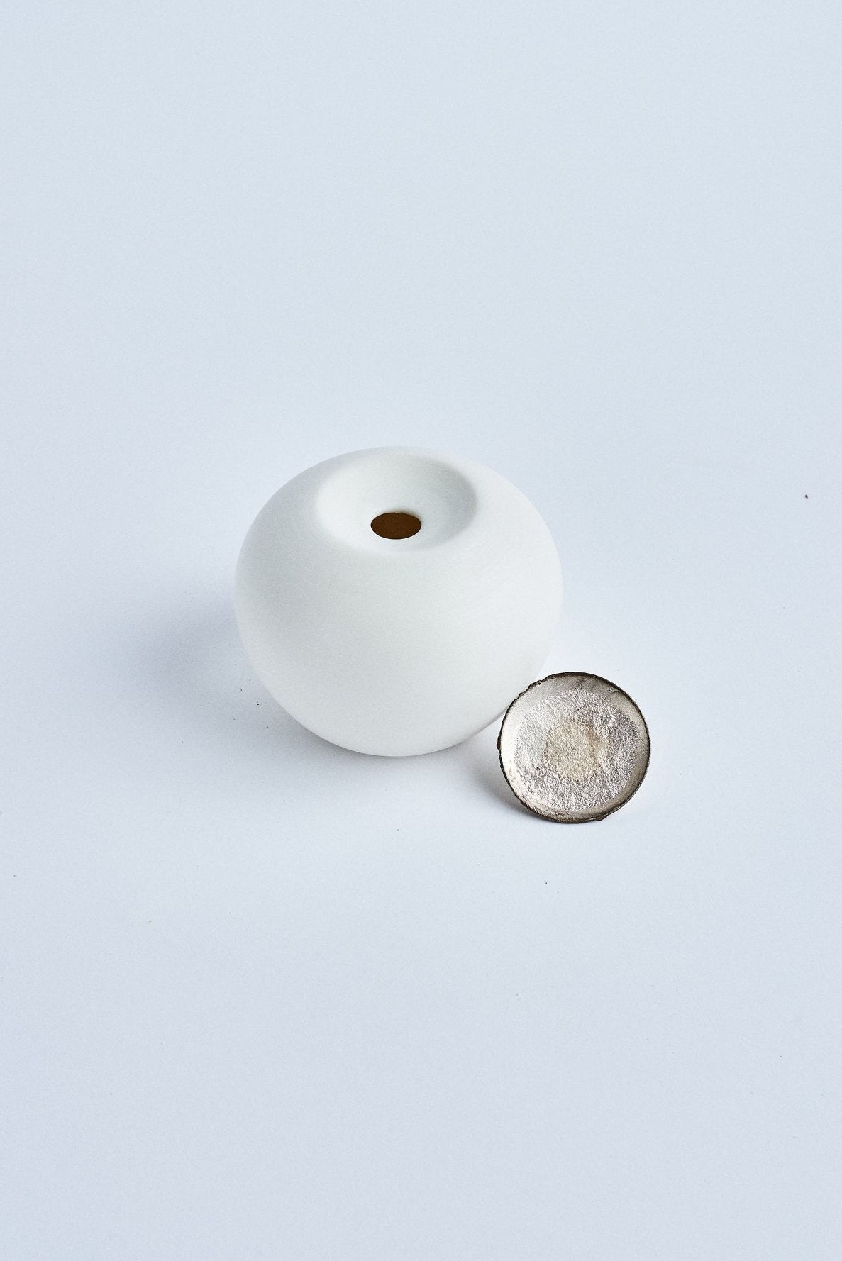 Pandora ouverte, vue de dessus : globe en porcelaine laissant deviner le verre fondu à l'intérieur, coupelle en argent recyclé posée à côté